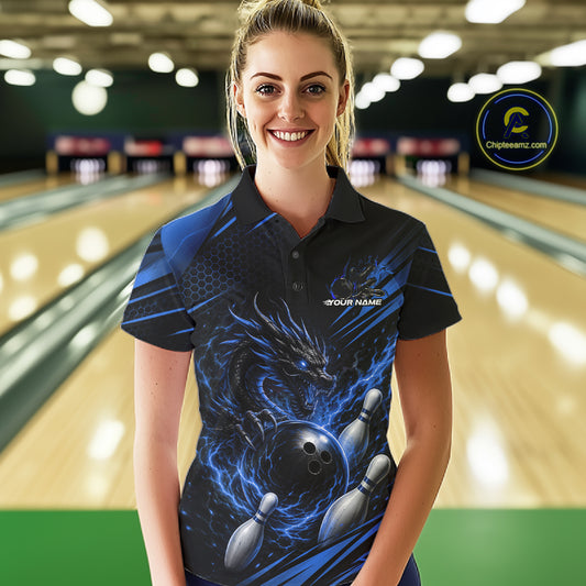 A woman stands in a bowling alley wearing a black short-sleeve polo shirt with a blue dragon and bowling ball graphic.