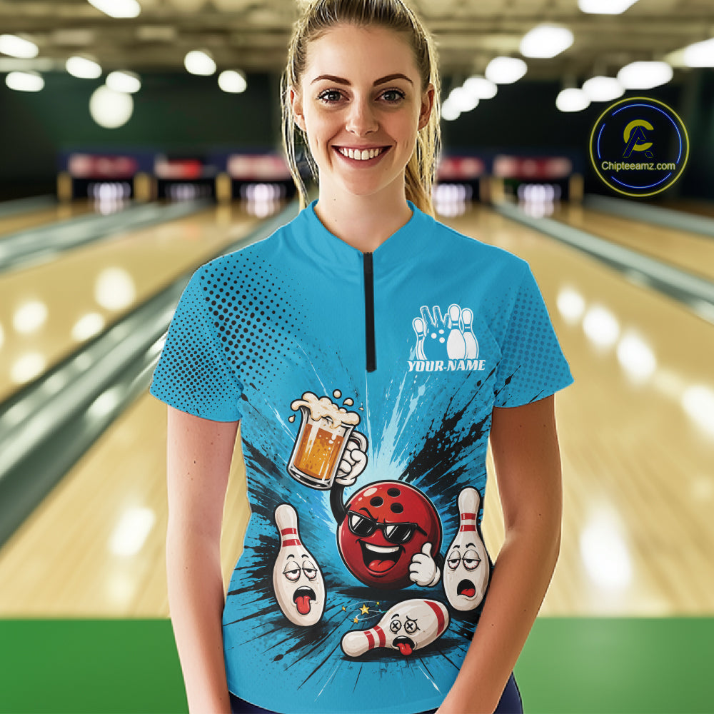 A woman stands in a bowling alley wearing a bright blue short-sleeve quarter-zip bowling shirt with a cartoon bowling graphic and the text 'YOUR NAME' on the chest.