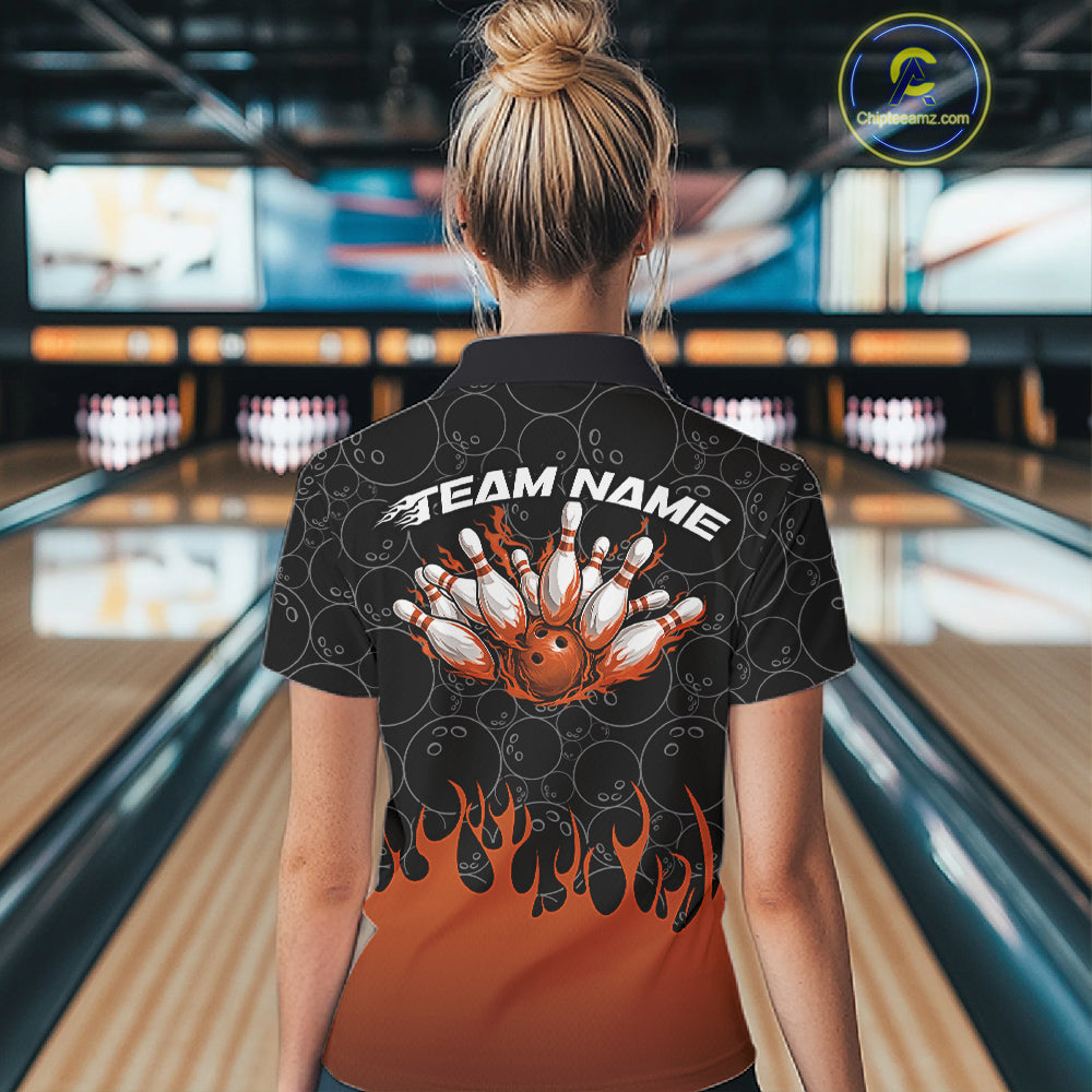 Back view of a female model in a bowling lane wearing a black polo shirt featuring vibrant orange flames and bowling ball pattern with bold athletic bowling graphics.