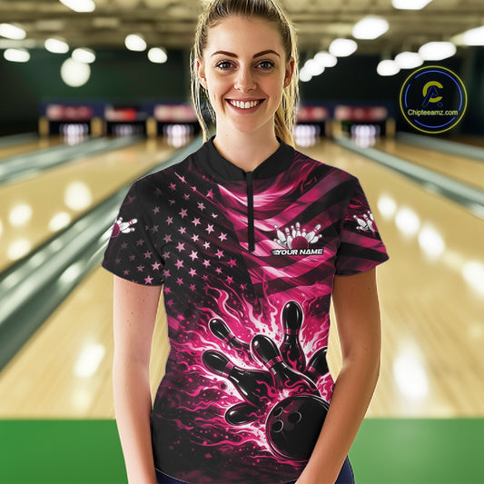 Female model wearing a black bowling quarter-zip shirt at the lane with pink flame bowling graphics and distressed flag accents.