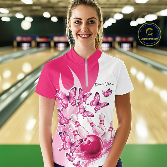 Female model wearing a white and pink bowling quarter zip with butterfly graphics and bowling artwork, front view at the bowling lane