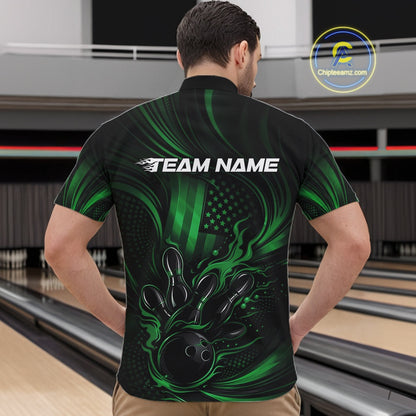 Front view of a male model in a bowling center wearing a black and green quarter-zip shirt featuring flaming bowling ball artwork and patriotic pin graphics.