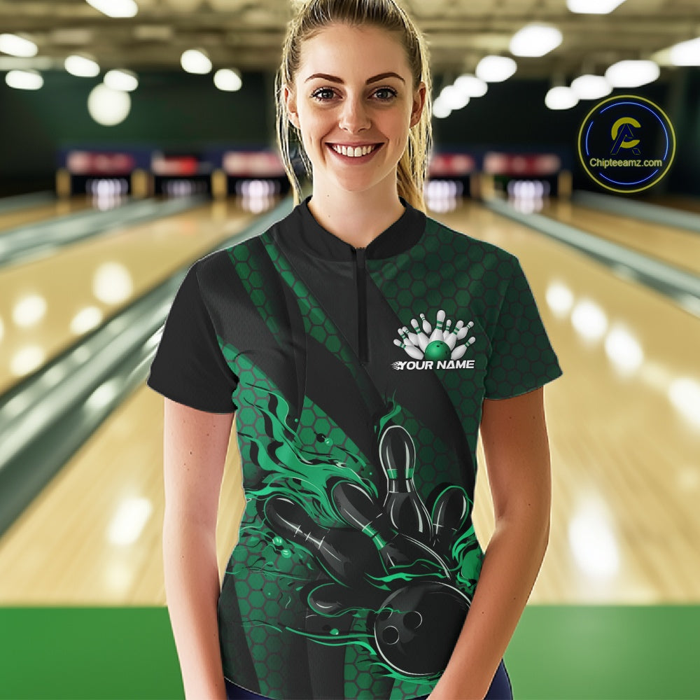 Female model in a bowling lane wearing black and green quarter zip shirt, front view featuring flaming bowling ball hitting pins with geometric stripe accents