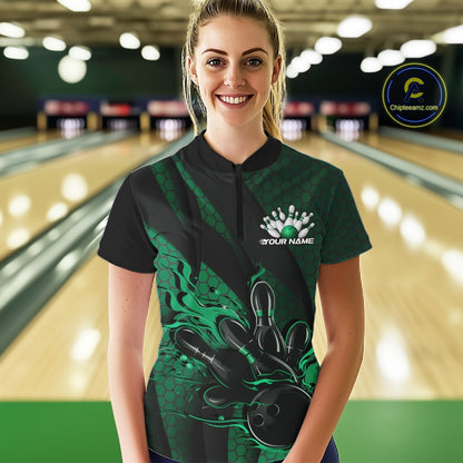 Female model in a bowling lane wearing black and green quarter zip shirt, front view featuring flaming bowling ball hitting pins with geometric stripe accents
