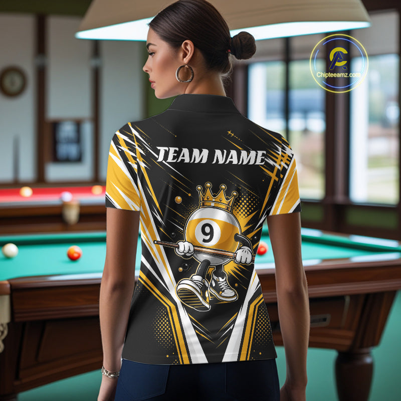 A woman stands in a billiards room wearing a custom black and yellow billiard polo shirt with crowned 9-ball cartoon character