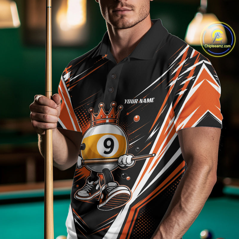 A man wearing a custom black and orange polo shirt with a crowned 9-ball billiard graphic on the front, holding a pool cue in a dimly lit pool hall. 