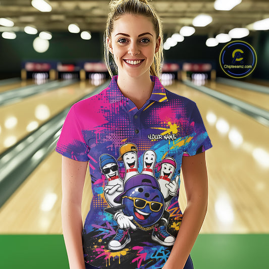 A woman stands in a bowling alley wearing a short-sleeve bowling polo shirt with a colorful graffiti-style design and cartoon bowling pins. 