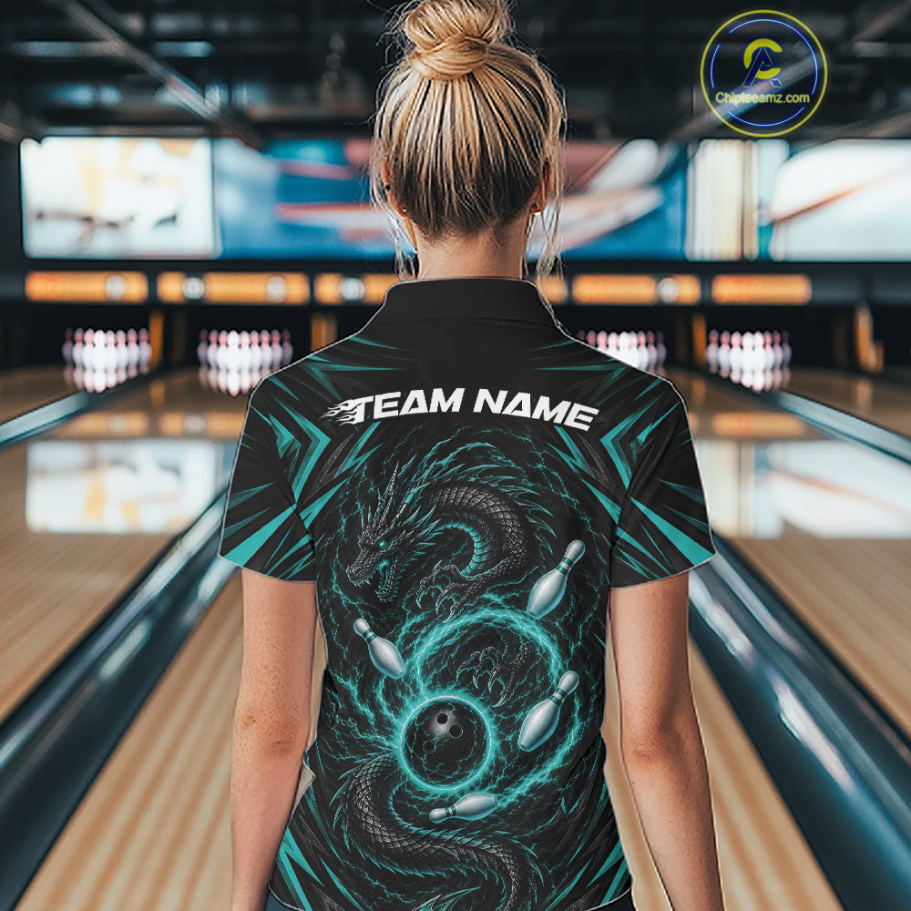 A woman viewed from behind wearing a black bowling-themed short-sleeve collared shirt with a large teal and black dragon graphic and the text 'TEAM NAME' across the upper back. The background shows a blurred bowling alley interior with lanes and pins.