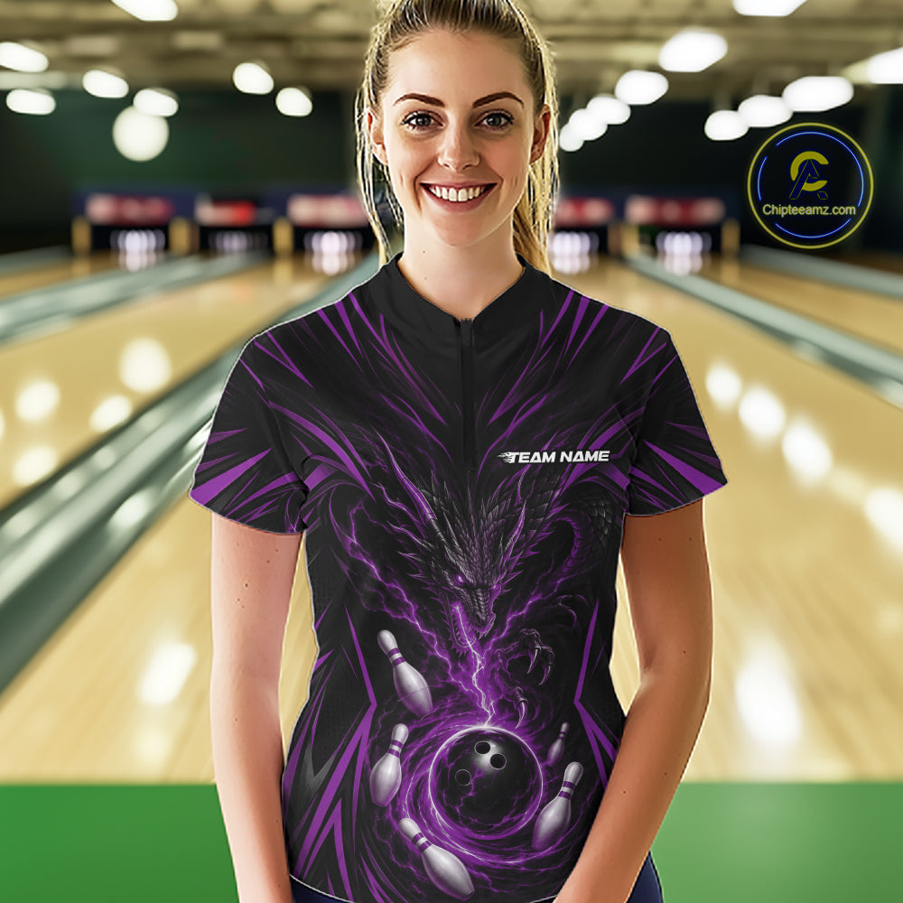 A woman stands in a bowling alley wearing a black short-sleeve bowling shirt with a purple and black lightning-bolt graphic and a white 'TEAM NAME' chest print. Bowling lanes are blurred in the background, and a circular 'Championship.