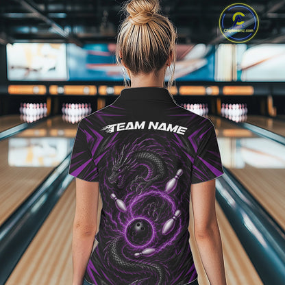 A woman viewed from behind wearing a black short-sleeve bowling quarter zip shirt with a purple dragon and bowling pin graphic on the back, standing in a bowling alley. The shirt has 'TEAM NAME' printed across the upper back