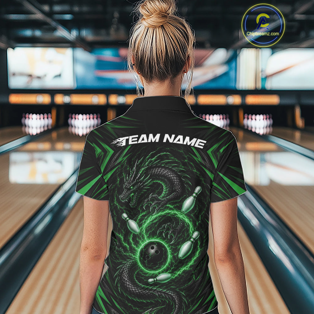 A woman viewed from behind wearing a black bowling-themed short-sleeve polo shirt with a green dragon and bowling ball graphic, and the text 'TEAM NAME' across the shoulders. The background shows a blurred bowling alley with lanes and pins.