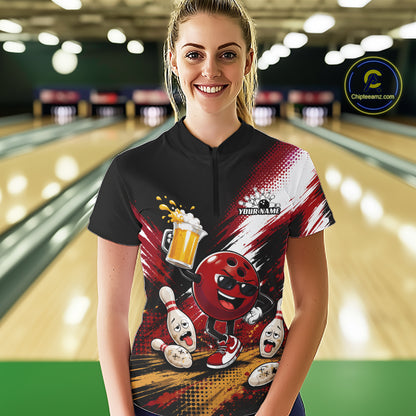 A woman stands in a bowling alley wearing a short-sleeve quarter zip shirt with a bold bowling-themed graphic print. The shirt is black on the upper chest and sleeves, with red, white, and yellow graphics including a cartoon bowling ball, bowling pins, bowling pins falling, a beer mug
