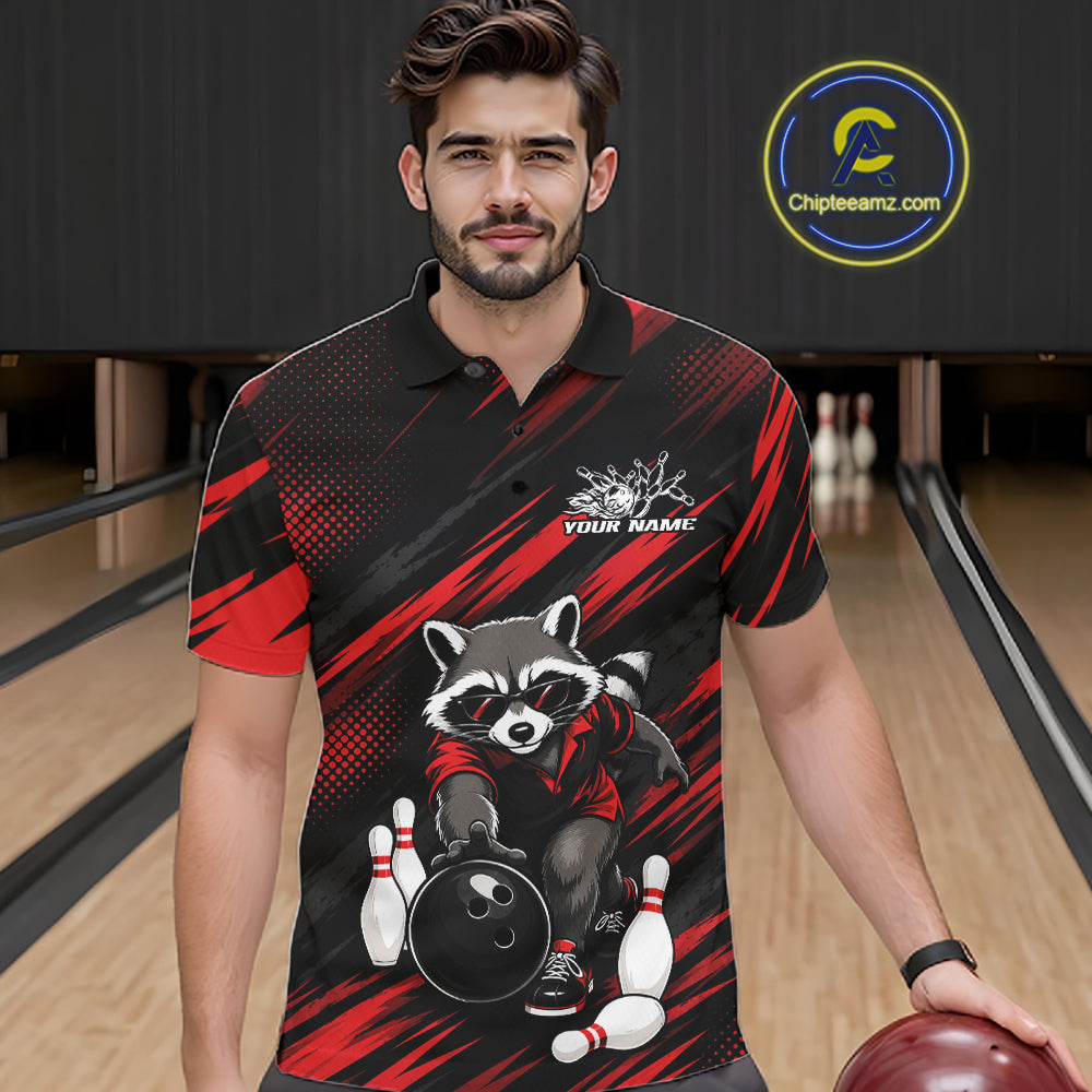 A man wearing a black and red bowling-themed polo shirt with a raccoon graphic, standing in a bowling alley holding a bowling ball. 