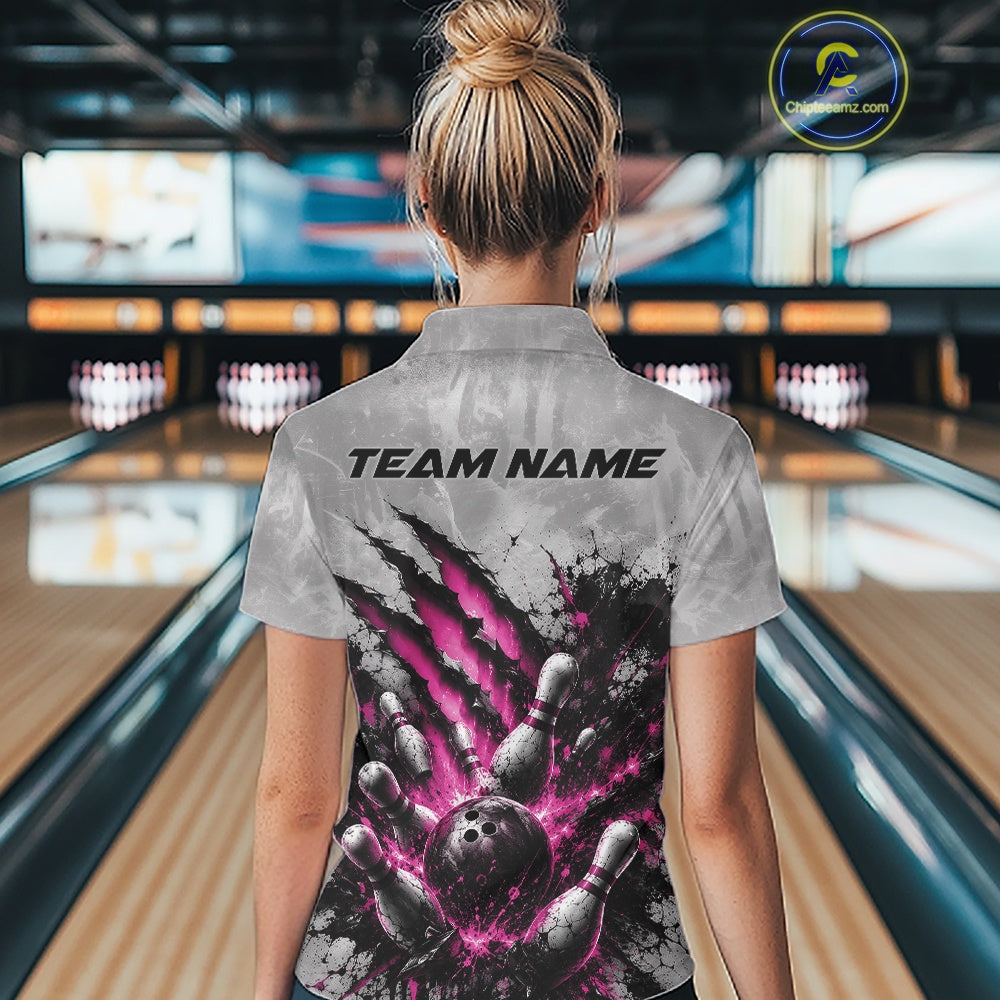 Back view of a female model wearing a gray bowling quarter zip shirt showcasing a dramatic pink bowling ball and pins graphic with claw-mark artwork in a bowling lane.