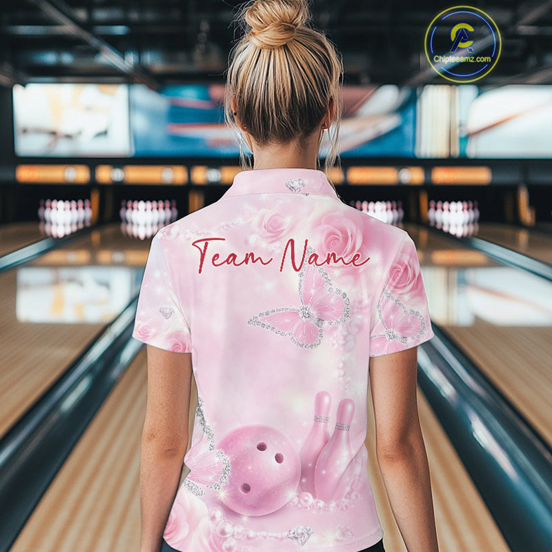 Back view of a female model in a bowling center wearing a quarter-zip bowling shirt with pink glitter butterflies, roses, bowling pins, and bowling graphics.