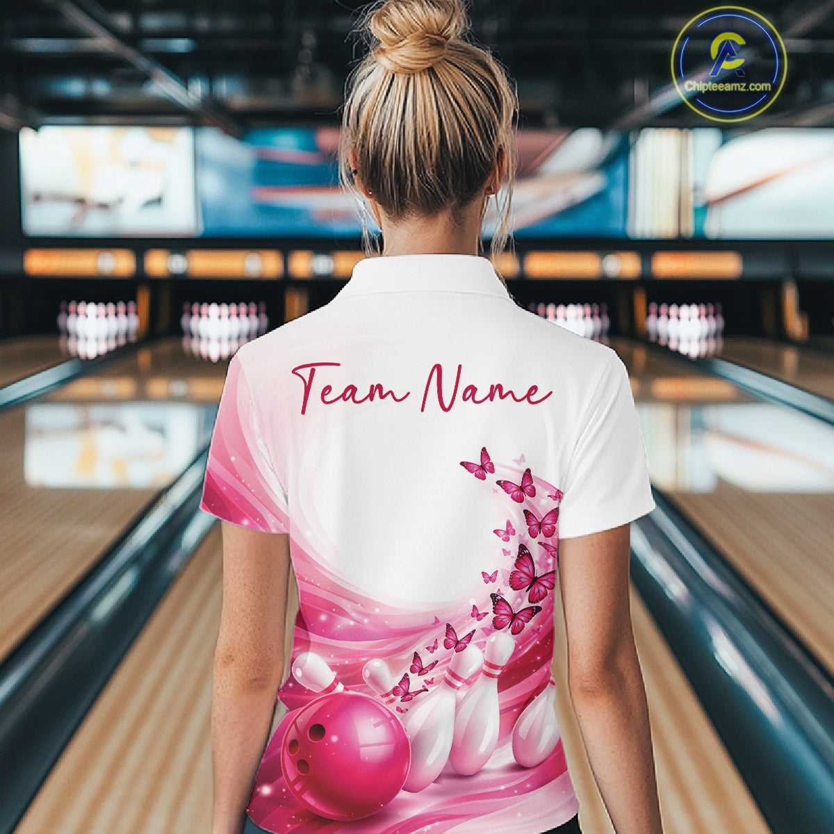 Back view of a women s white and pink bowling quarter zip displaying butterfly artwork and bowling-themed graphics inside a bowling alley.