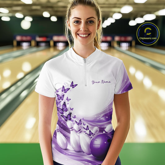 Female model wearing a white and purple bowling quarter zip featuring butterfly artwork and bowling-themed graphics in a bowling venue.