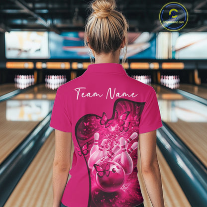 Female model in a pink bowling polo with butterfly graphics and bowling artwork, back view inside a bowling center