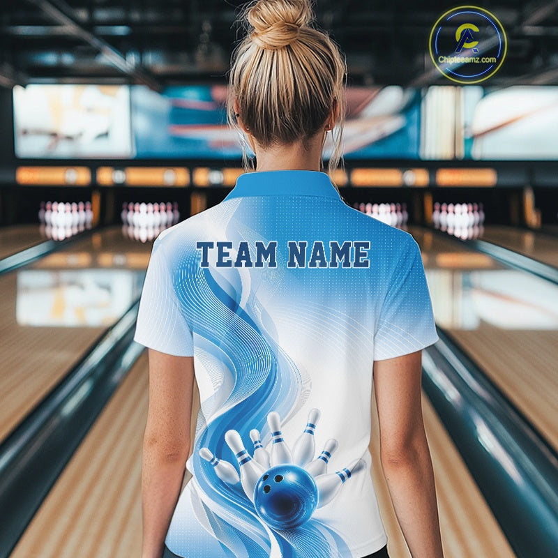 Female model standing in a bowling lane showing the back of a white and blue bowling quarter-zip shirt with abstract wave lines and a glossy bowling ball striking pins graphic.