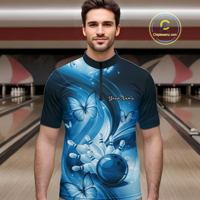 Male model in a bowling alley wearing a blue quarter-zip shirt with bowling ball and butterfly-themed artwork.