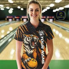 Load image into Gallery viewer, Front view of a female model at a bowling lane wearing a black and yellow bowling polo shirt featuring a roaring tiger holding a yellow bowling ball with orange claw-stripe graphics and a geometric background pattern.