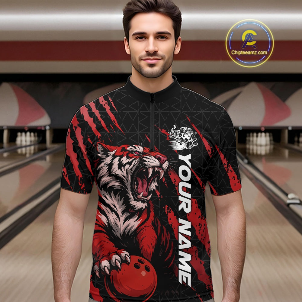 Front view of a male model at a bowling lane wearing a black and red bowling quarter-zip shirt featuring a roaring tiger holding a red bowling ball with matching red claw-stripe artwork and a geometric background pattern.