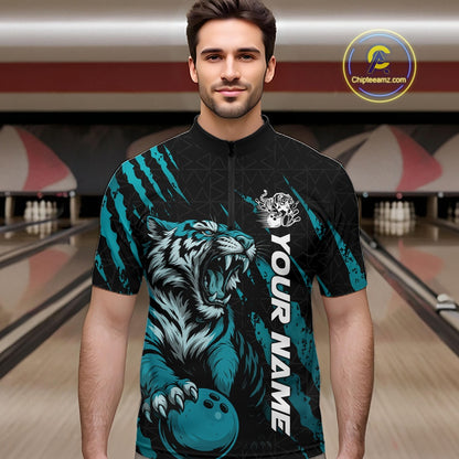 Front view of a male model at a bowling lane wearing a black and teal blue bowling quarter-zip shirt showcasing a roaring tiger holding a teal blue bowling ball with matching claw-stripe graphics and a geometric background pattern.