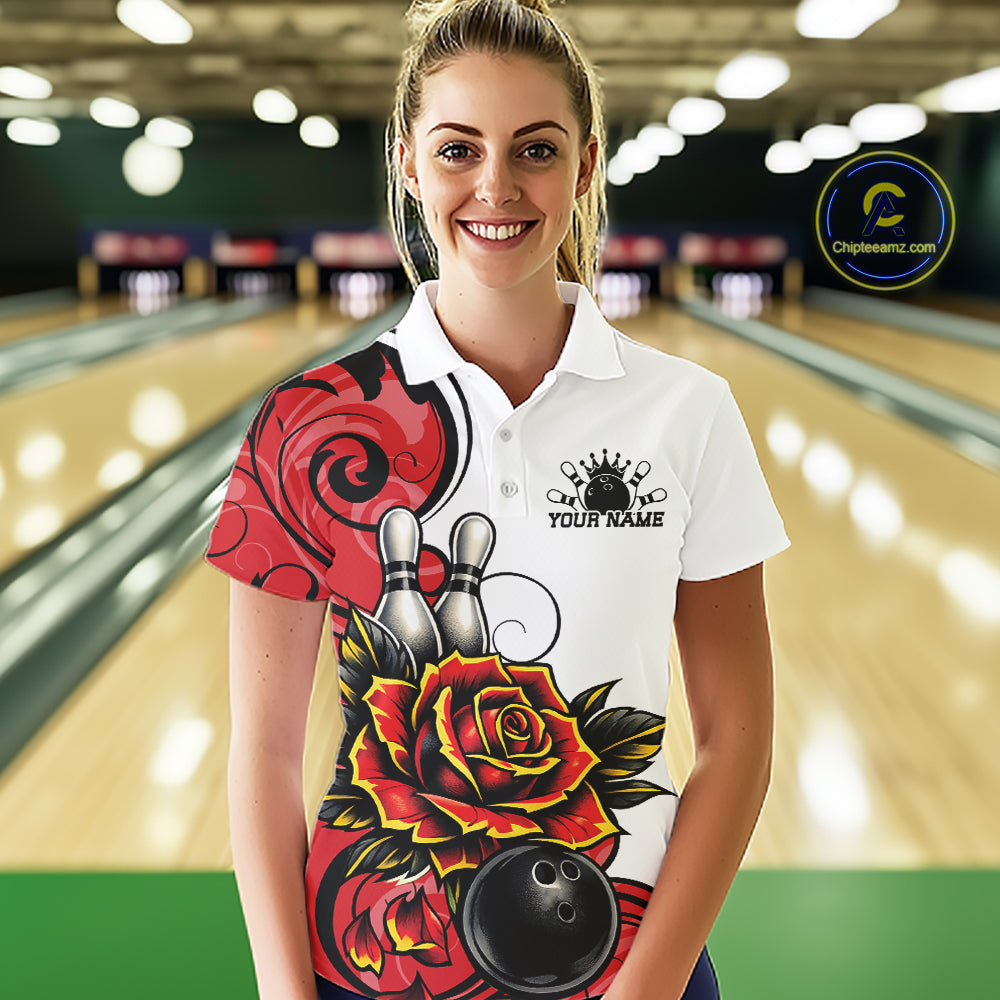 A woman stands in a bowling alley wearing a white short-sleeve polo shirt with a large red, black, and yellow rose graphic and bowling pins on the front. 