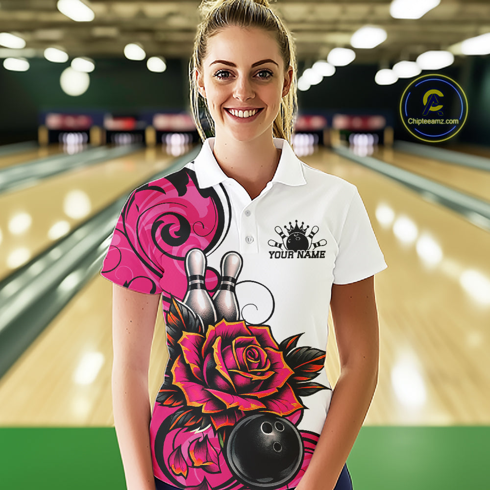 A woman stands in a bowling alley wearing a white short-sleeve polo shirt with a large pink and black floral graphic, bowling pins, and a bowling ball design.