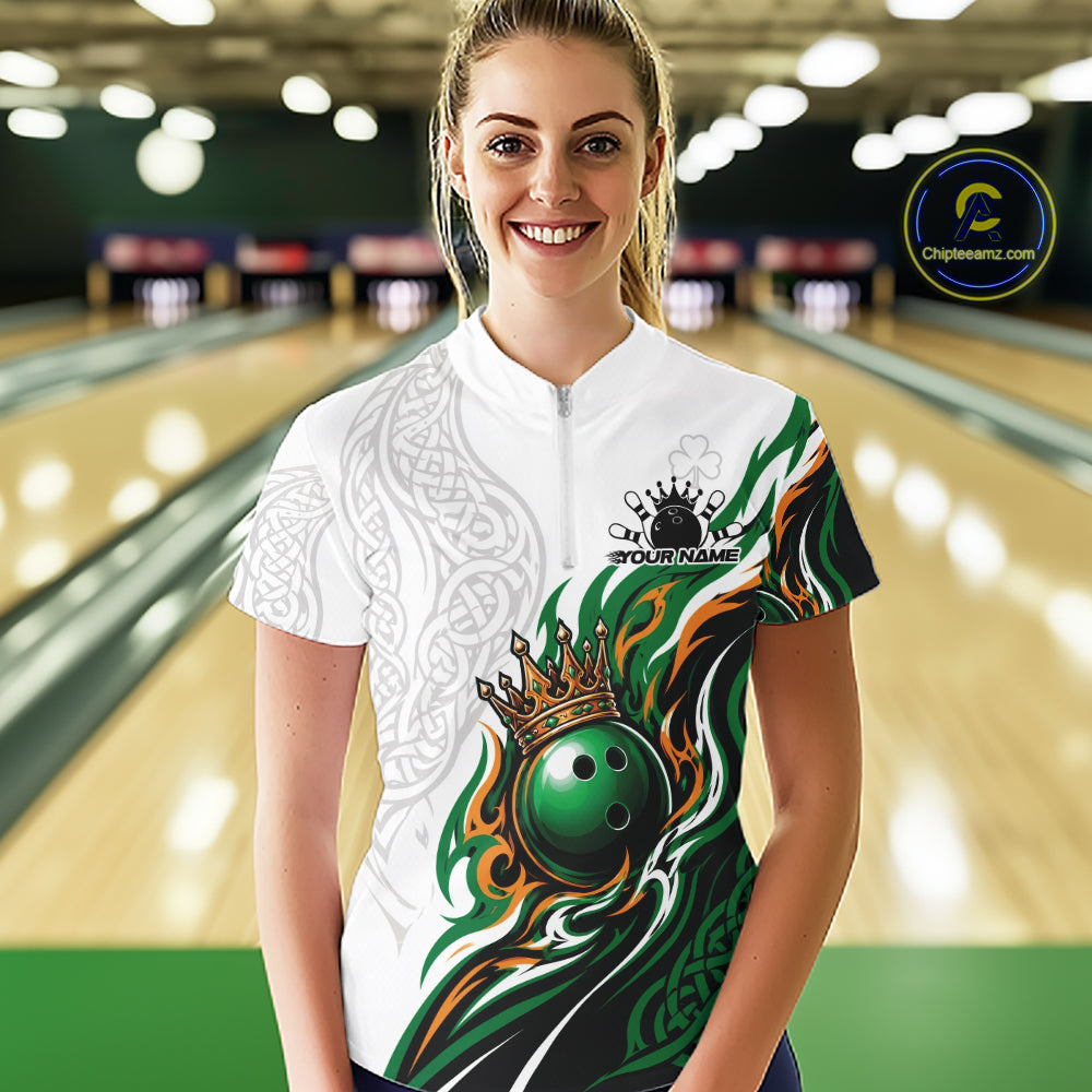 A woman wearing a custom short-sleeve bowling quarter zip shirt with a white base, green and orange flame graphics, a crown and bowling ball design, and a white Celtic knot pattern on the sleeve. 