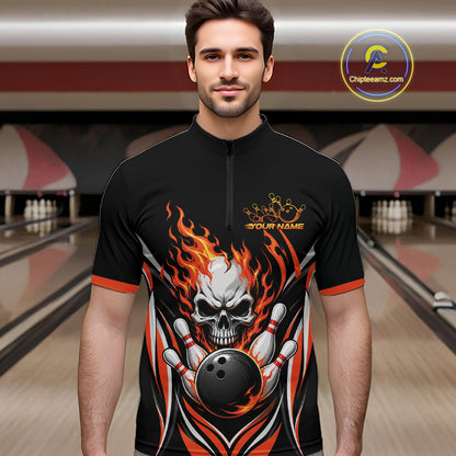 A man wearing a black short-sleeve bowling quarter zip shirt jersey with a large skull and flame graphic on the front, standing in a bowling alley. The jersey has orange and white flame details, a white skull holding bowling pins, a black bowling ball
