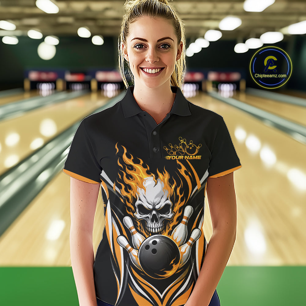 A woman stands in a bowling alley wearing a black short-sleeve polo shirt with a large skull-and-flame graphic and bowling-themed print. 