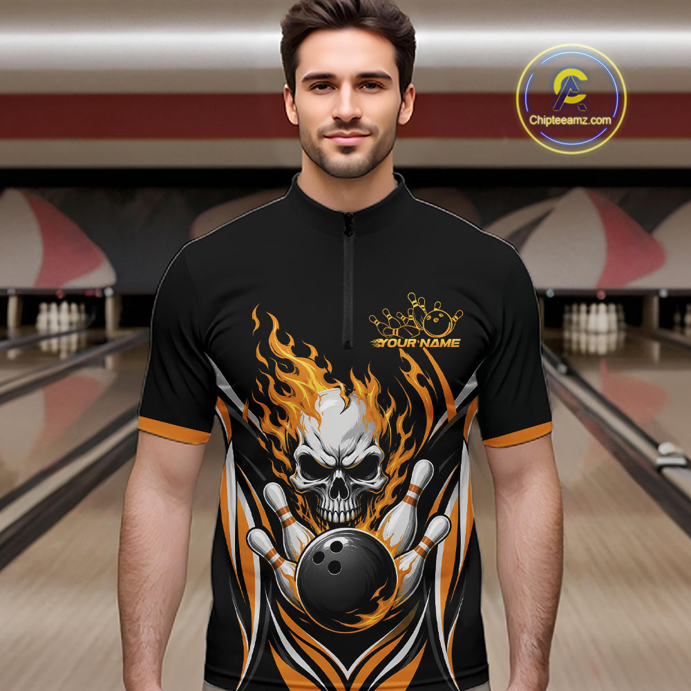 A man wearing a black short-sleeve bowling quarter zip shirt jersey with a large skull and flame graphic on the front, standing in a bowling alley. The jersey has orange and white flame details, a black bowling ball graphic, and 'YOUR NAME' printed on the chest.