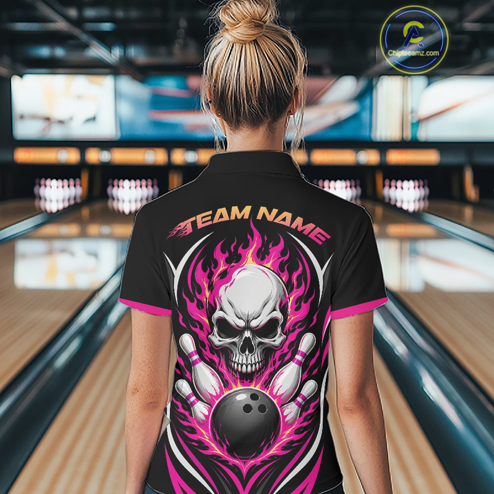 A woman viewed from behind wearing a black bowling shirt with a large skull and flame graphic on the back, standing in a bowling alley. 