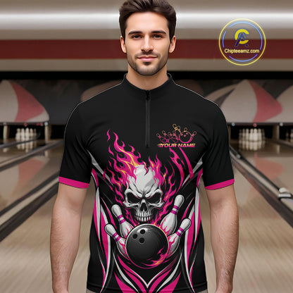 A man wearing a black short-sleeve bowling quarter zip shirt with a large skull and bowling ball graphic in pink, white, and gray, standing in a bowling alley.