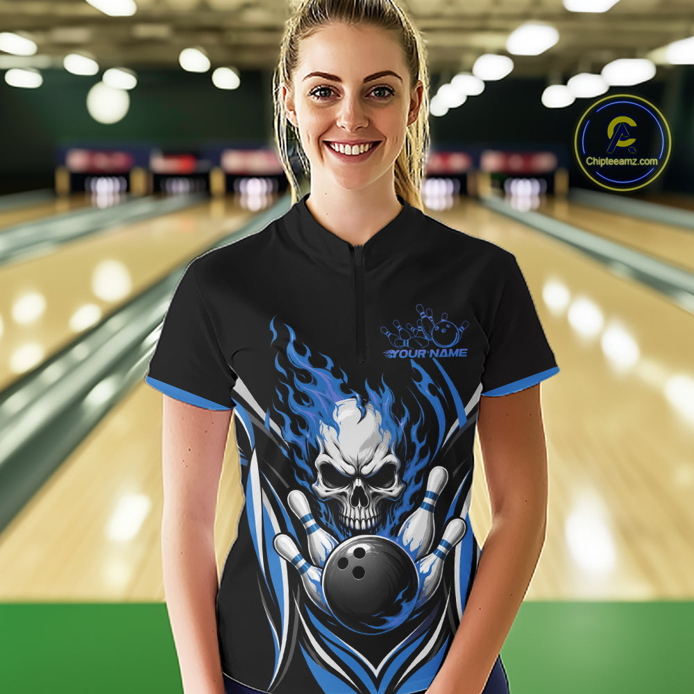 A woman stands in a bowling alley wearing a black short-sleeve bowling quarter zip shirt with a large skull-and-bowling-ball flame graphic 