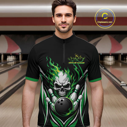 A man wearing a black short-sleeve bowling quarter zip shirt with a green and white skull-and-bowling-ball flame graphic, standing in a bowling alley. 