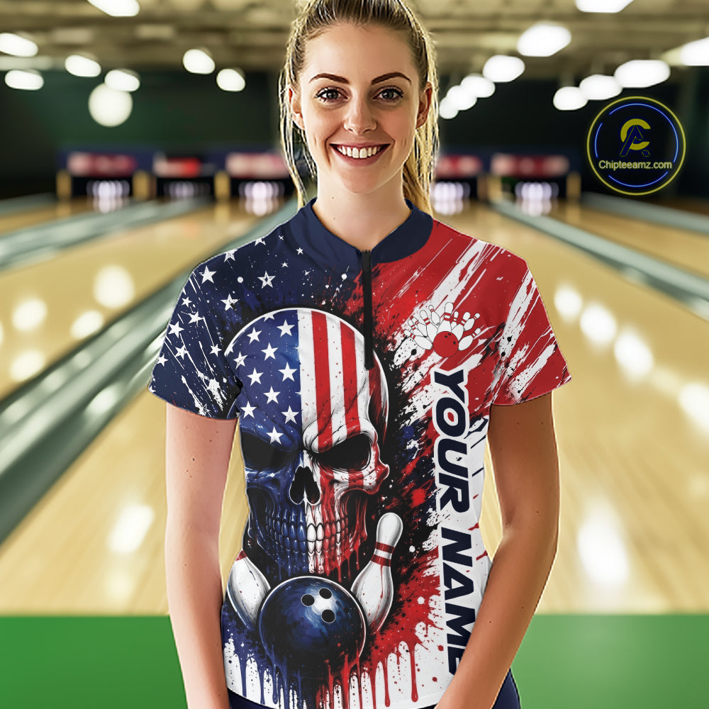 A woman standing in a bowling alley wearing a short-sleeve custom bowling quarter zip shirt with a patriotic red, white, and blue design featuring a skull and bowling pins.