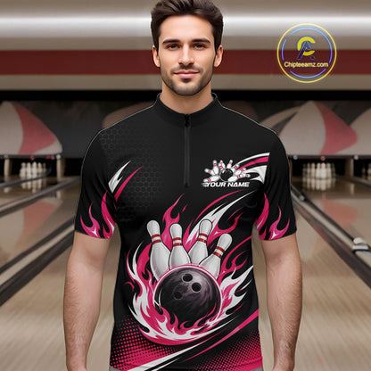 A man wearing a black short-sleeve bowling quarter zip shirt with a pink, white, and black flame and bowling pin graphic, standing in a bowling alley.