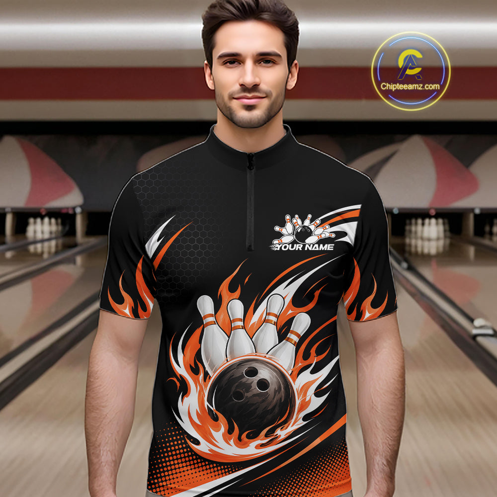 A man wearing a black short-sleeve bowling quarter zip shirt with a black and orange flame and bowling graphics, standing in a bowling alley. 