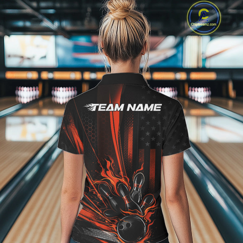 Back view of a female model in a bowling center wearing a black and orange quarter-zip shirt featuring a bowling strike scene with patriotic details.