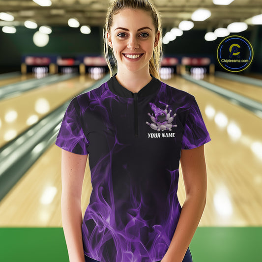 Female model at a bowling lane wearing a black and purple bowling quarter-zip shirt with bowling strike artwork and flame-inspired details.