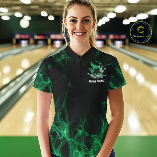 Female model at a bowling lane wearing a black and green bowling quarter-zip shirt with bowling strike artwork, scattered pins, and flame effects.