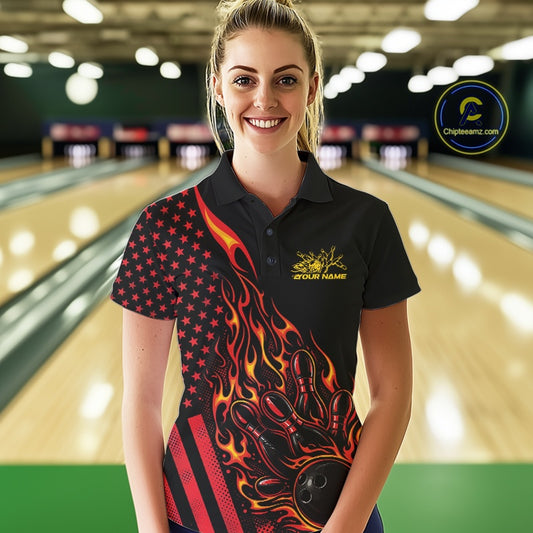Female model at a bowling lane wearing a black bowling polo shirt with red-orange flame bowling strike artwork and patriotic graphics.