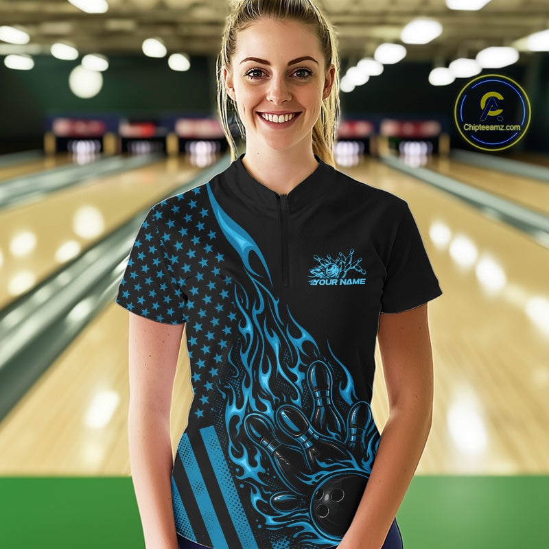 Female model wearing a black bowling quarter-zip shirt at a bowling lane with blue flame bowling action artwork and patriotic accents.
