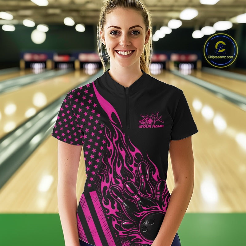 Female model wearing a black bowling quarter-zip shirt at a bowling lane with a pink flaming bowling ball knocking down pins and patriotic graphics.