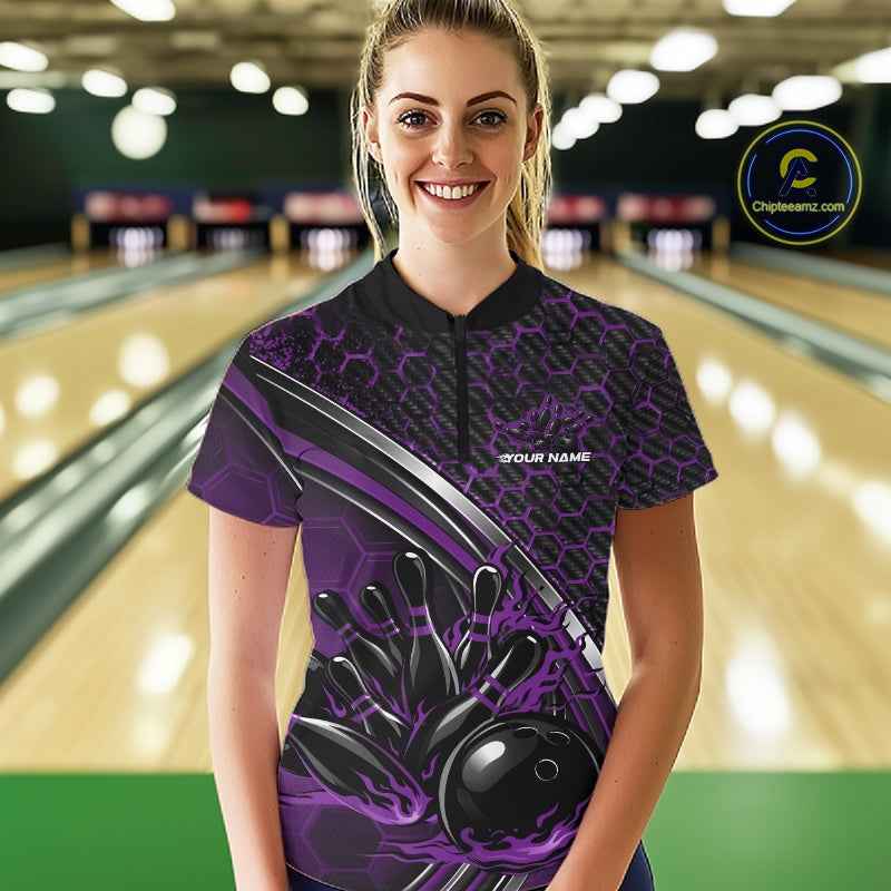 Female model wearing a black and purple bowling quarter zip with honeycomb artwork and flaming bowling ball striking pins inside a bowling alley.