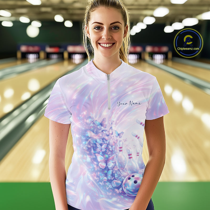 Female model wearing a bowling quarter zip with pastel holographic butterfly artwork and bowling graphics, front view inside a bowling alley