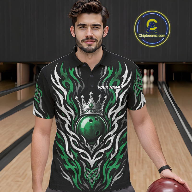A man wearing a black short-sleeve bowling-themed polo shirt with a green and white tribal flame design and a crown graphic, standing in a bowling alley. 