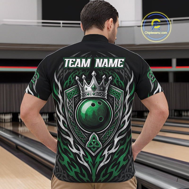 A man viewed from behind wearing a black bowling short sleeve quarter zip shirt with a large green and crowned bowling ball on the back, standing in a bowling alley.